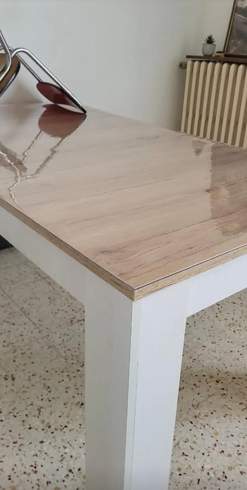 Licht tafelblad op witte poten met de glans van de mat; op de achtergrond een gietijzeren radiator