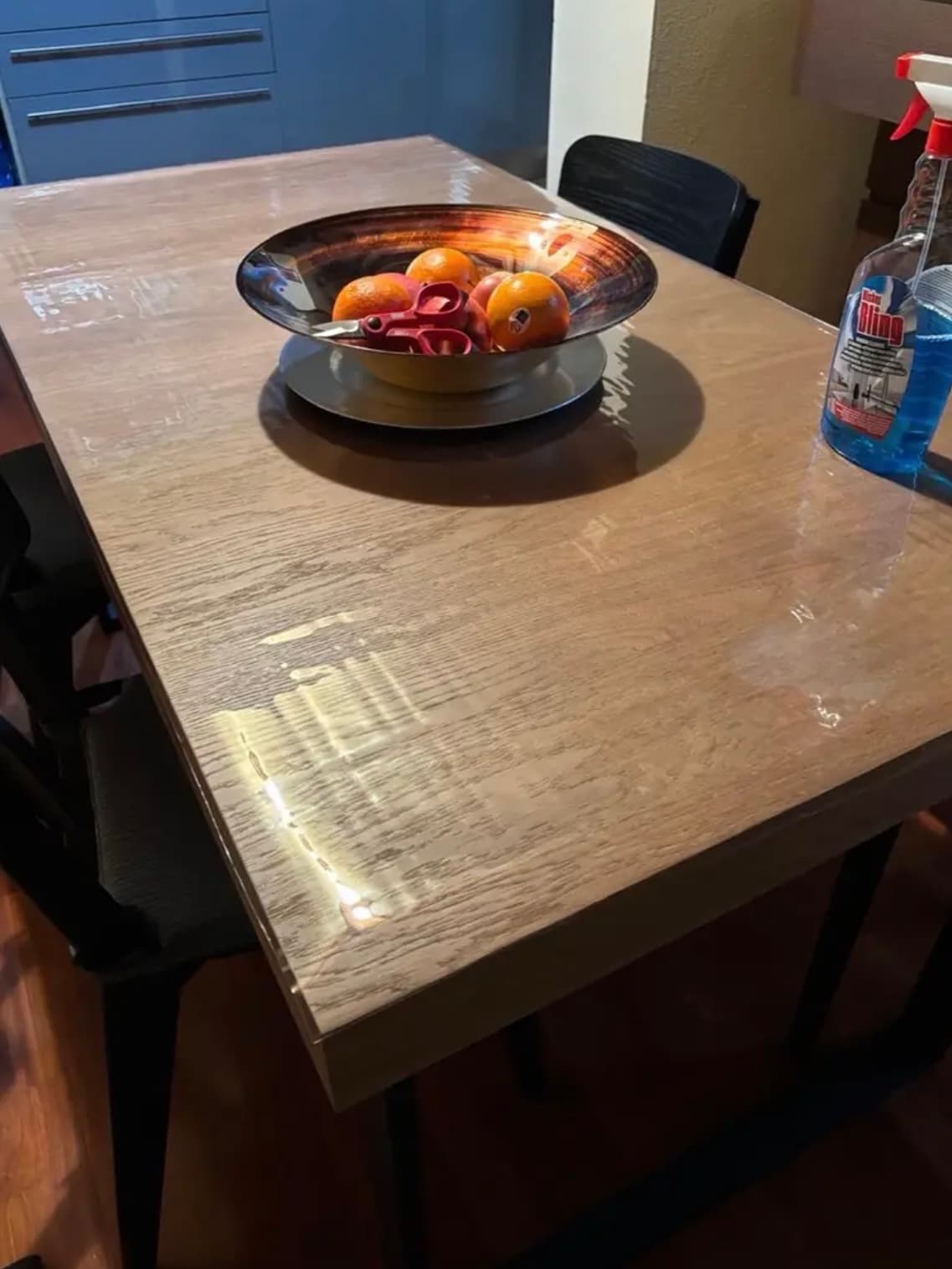 Metalen schaal met sinaasappels op een eiken blad; naast de mat staat een fles glasreiniger