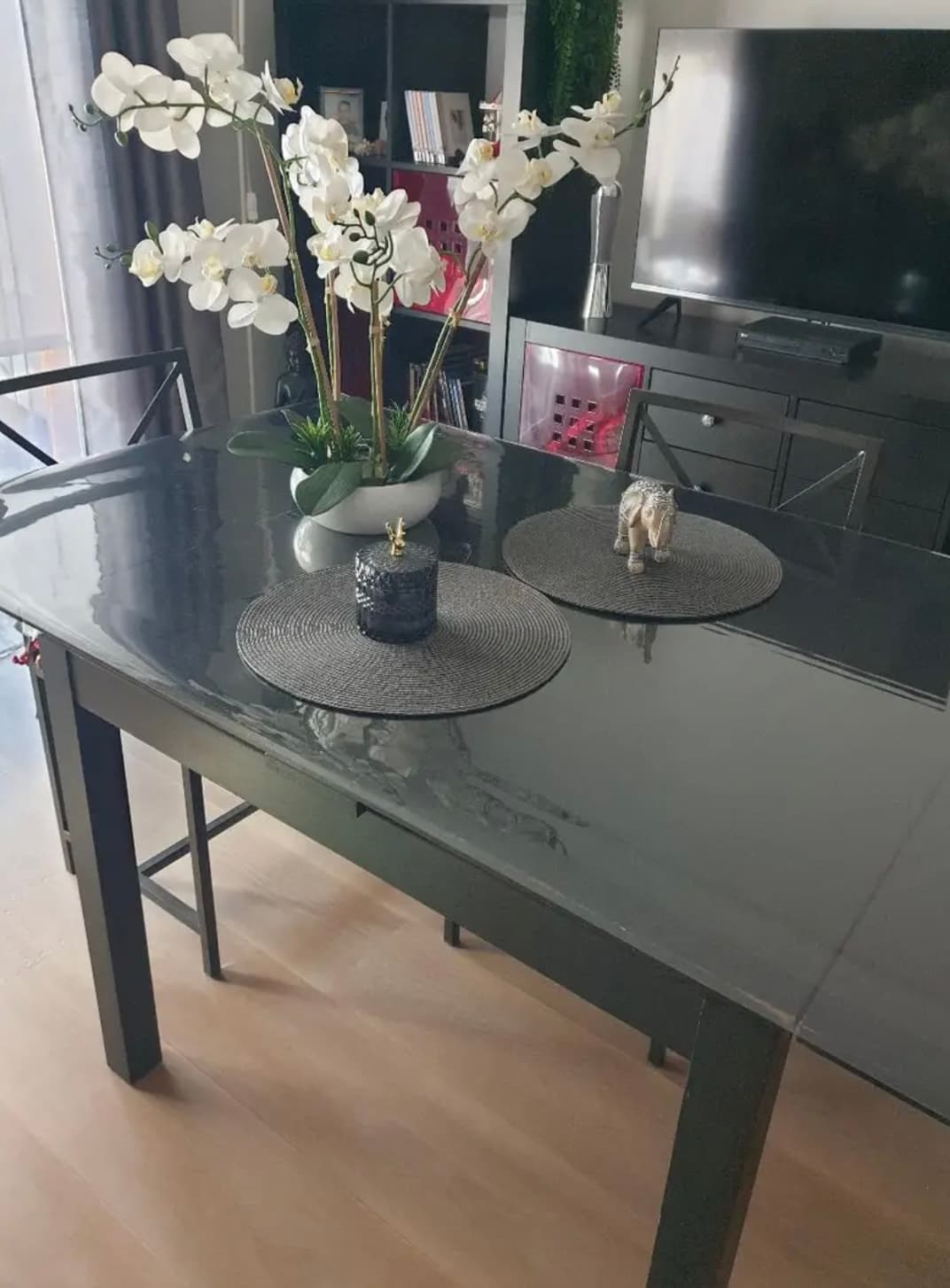 Grafietgrijze tafel in de woonkamer met een witte orchidee en ronde onderzetters, het blad onder de mat