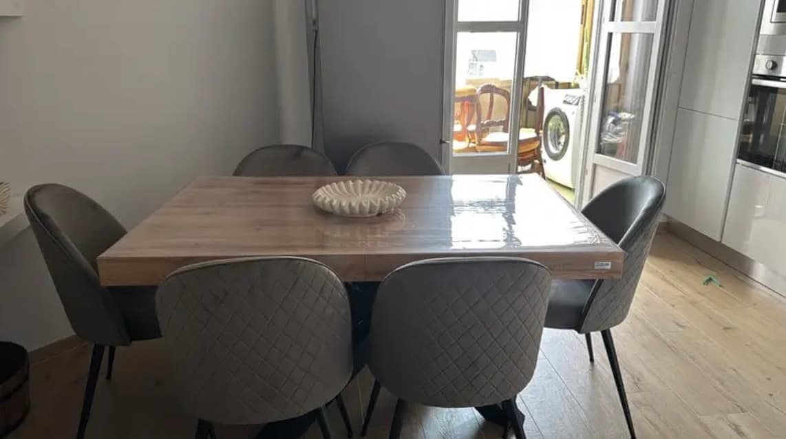 Keukentafel met zes grijze stoelen; op de net uitgerolde mat hangt nog het etiket