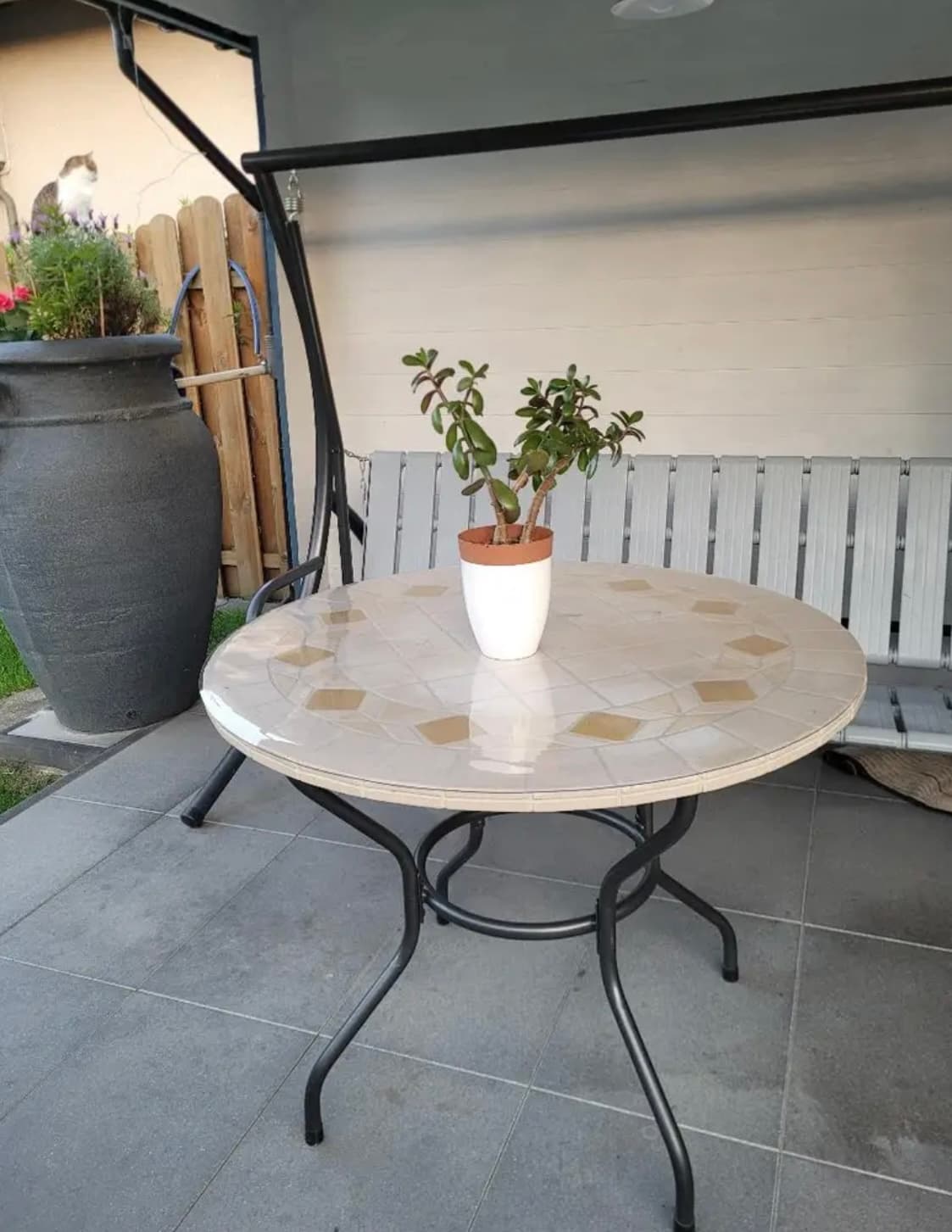Rond tafeltje met mozaïekblad op het terras, op de mat een pot met een geldboom