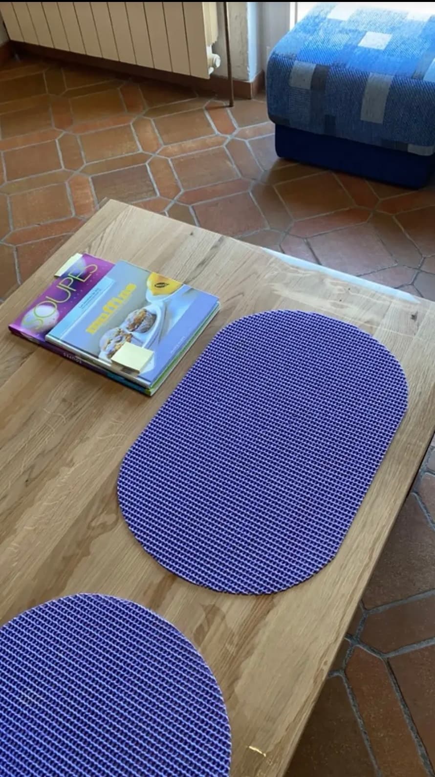 Eiken tafel met paarse placemats en kookboeken; de rand van de mat steekt buiten het blad
