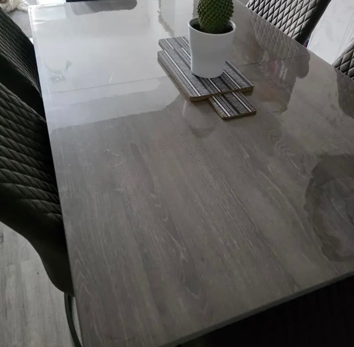 Grijs gebeitste tafel met een cactus op houten onderzetters, rondom gecapitonneerde stoelen