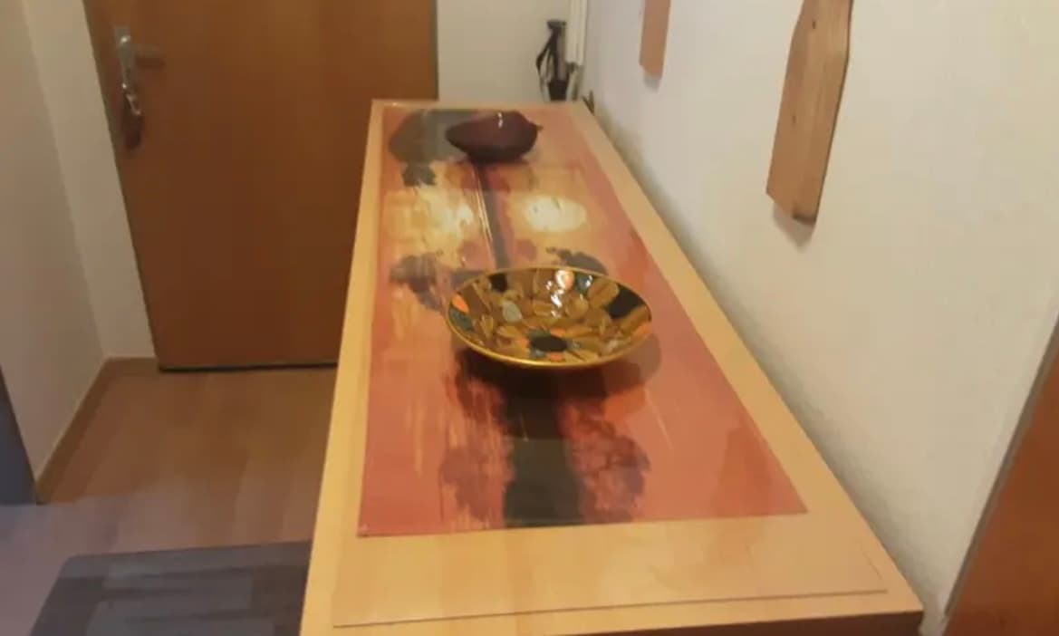 Smalle lichte tafel in de hal: onder de mat een rood patroon van het blad, erbovenop een messing schaal