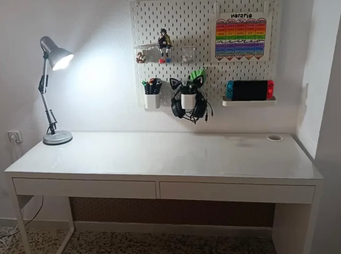 Wit bureau met een lamp en gereedschapsbord aan de muur; het blad wordt beschermd door een transparante afdekking